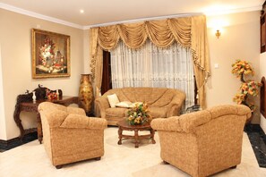 A living room with a sofa, two armchairs, a coffee table, a painting, a vase, and a lamp.