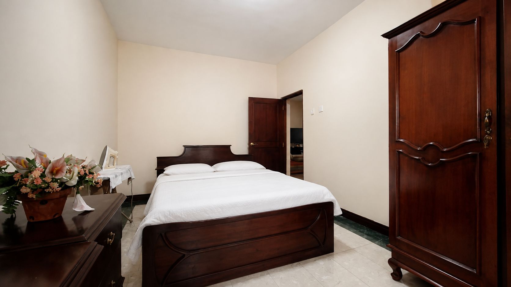 A bedroom with a bed, a wooden wardrobe, and a potted plant.