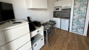 Uma cozinha compacta com armários brancos, micro-ondas, torradeira e uma pequena mesa de jantar.