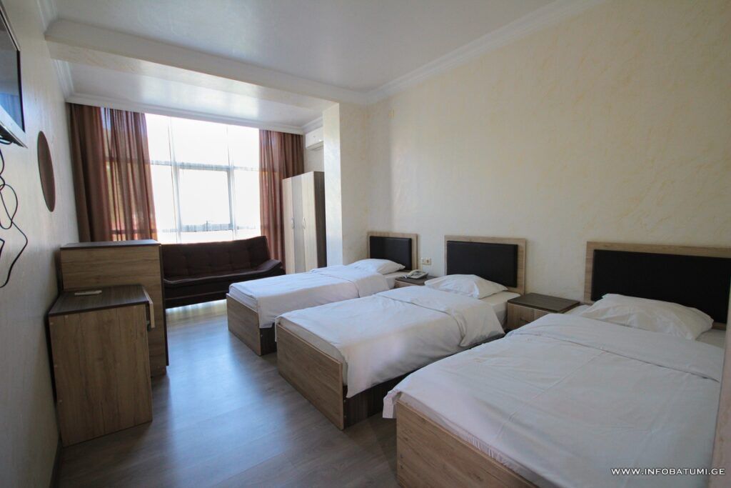 A hotel room with three single beds, a desk, and a small cabinet.