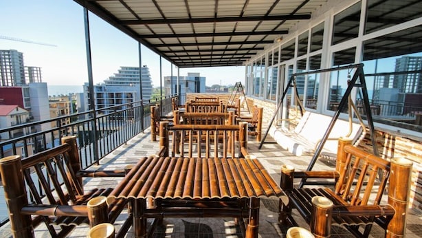A rooftop terrace with bamboo furniture and large windows offering a city view. - Hotel Temo (Batumi)