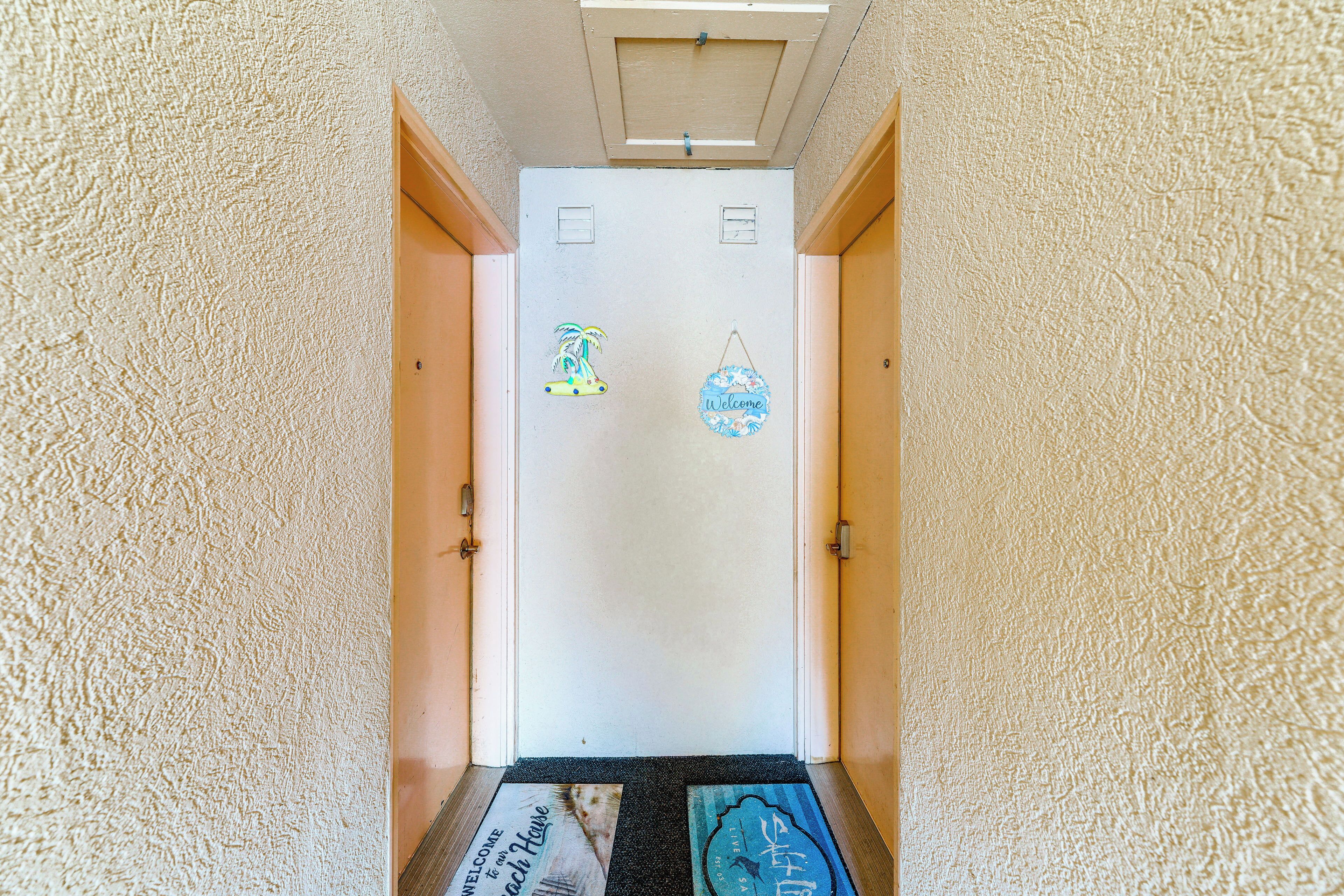 Un corridoio con pareti strutturate, una porta con il cartello 'Welcome' e un segnale con scritto 'Beach House' sul pavimento.