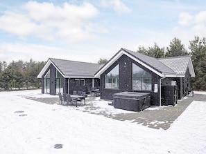 Eine moderne Blockhütte mit einer großen Terrassenfläche, einem Whirlpool und einer überdachten Sitzgruppe.