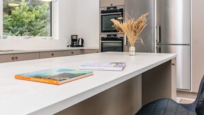 Een moderne keuken met een groot keukeneiland, roestvrijstalen apparatuur en uitzicht op groen.