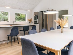 Une cuisine moderne dotée d’un îlot central, d’appareils électroménagers en acier inoxydable et d’un coin repas avec une longue table et des chaises.
