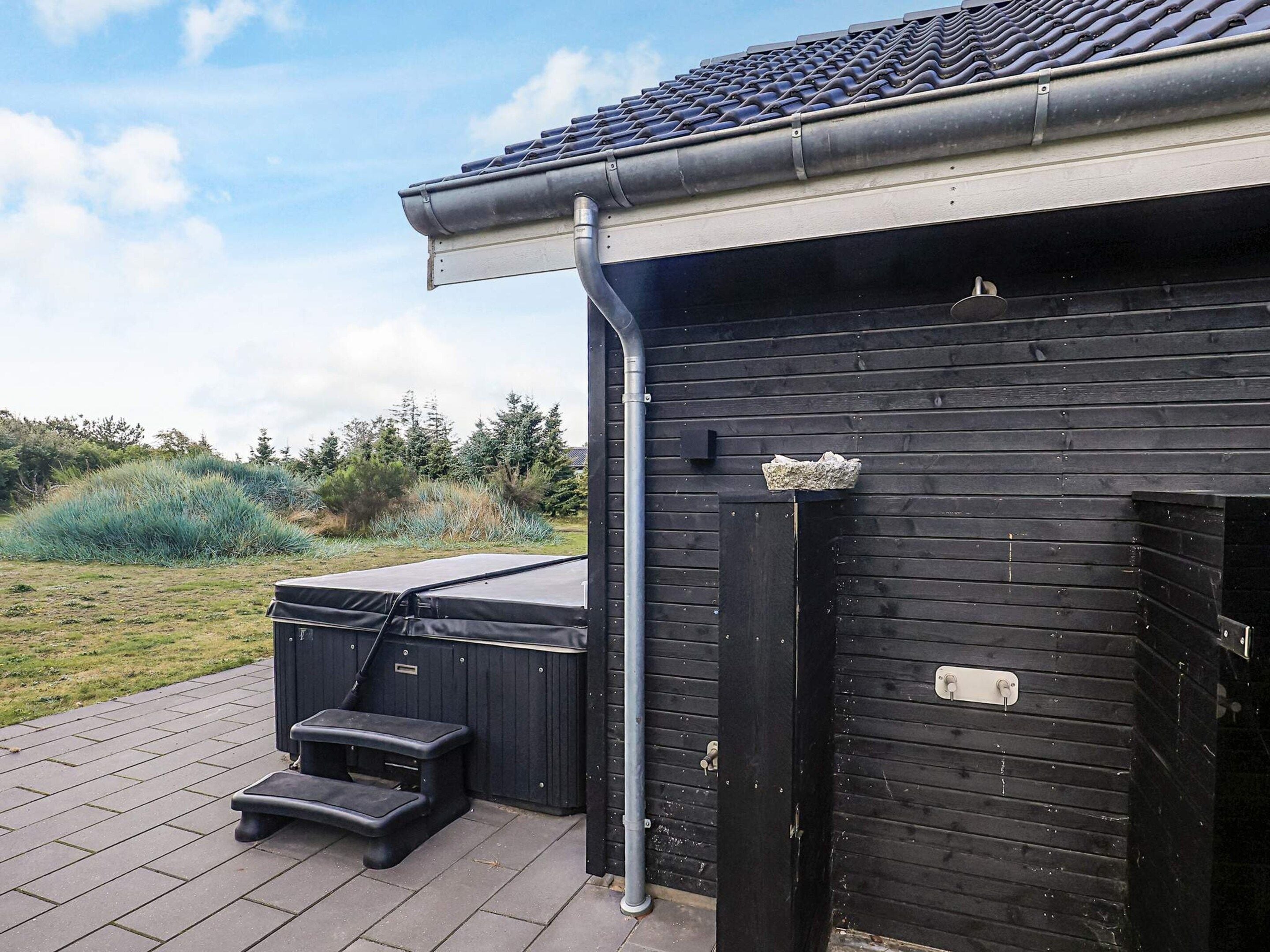 Een zwarte metalen constructie met dak, een klein buitgedeelte met treden, en een houten deur met een metalen plaat.