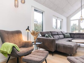 Un salon moderne comprenant un canapé d’angle, un fauteuil et une petite table d’appoint avec une lampe et un vase décoratif.