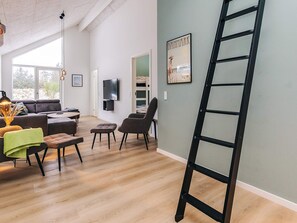 A modern living room with a sofa, chairs, a TV, and a ladder against a wall. - 5 Star Holiday Home in Blokhus (Blokhus)