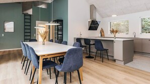 Een moderne keuken met een eethoek, met een lange tafel met stoelen, een keukeneiland en een raam met uitzicht op groen.