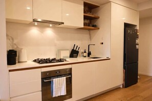 A modern kitchen with white cabinets, a stainless steel range, a built-in oven, and a black refrigerator.