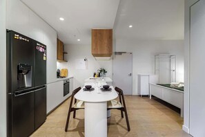 A modern kitchen with a central island, black refrigerator, and white cabinetry. - Premium South Melb 2 Queens + Study, Tram at door (Southbank)