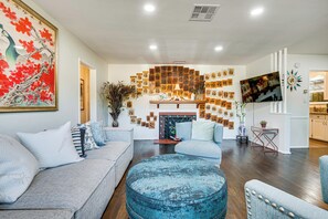 A modern living room with a sofa, ottoman, and a TV. There is a fireplace and a wall with calligraphy art. - 'peacock House Sanctuary' 4 Mi to Old Pasadena! (Pasadena)