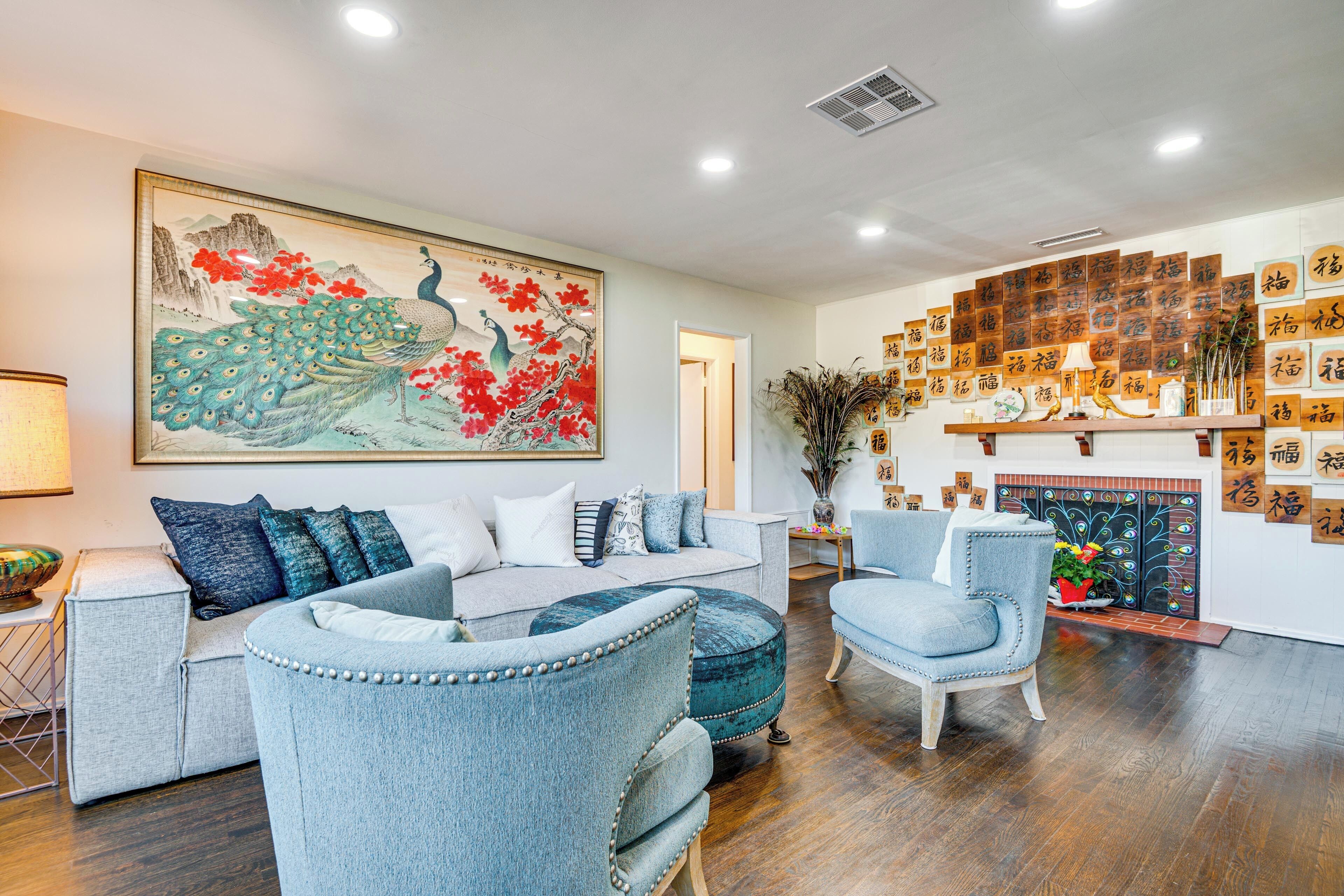 Un salon comprenant un canapé, deux fauteuils, une table basse, une cheminée agrémentée d’objets décoratifs et un mur orné de calligraphies.