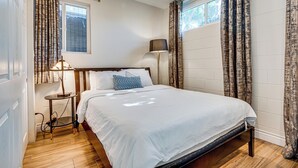 Un lit bien fait, avec une tête de lit en bois, une table de chevet avec une lampe et une fenêtre avec des rideaux.