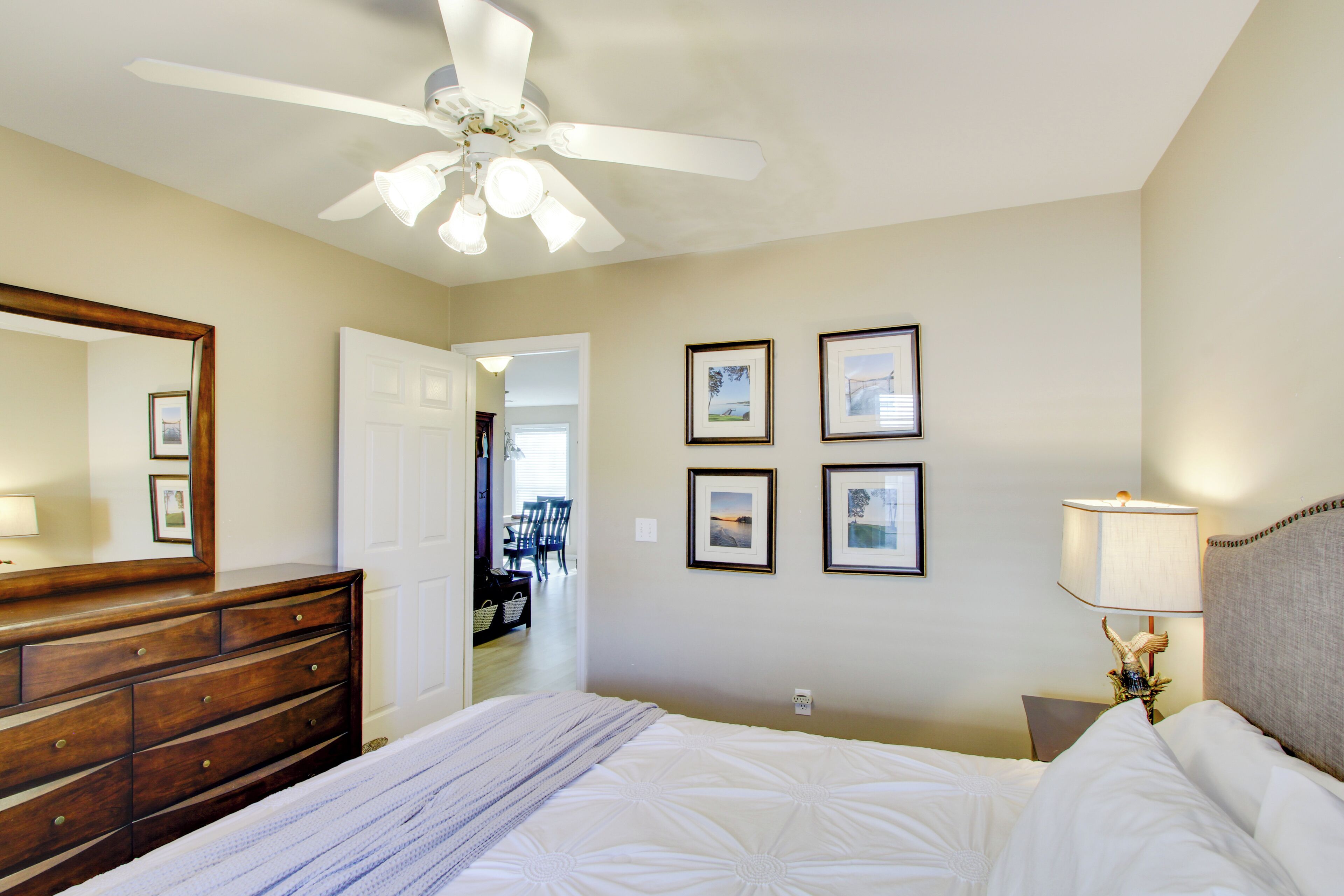 A hotel room with a bed, dresser, ceiling fan, wall-mounted lamps, and framed pictures.