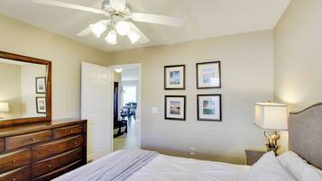 A hotel room with a bed, dresser, ceiling fan, wall-mounted lamps, and framed pictures.