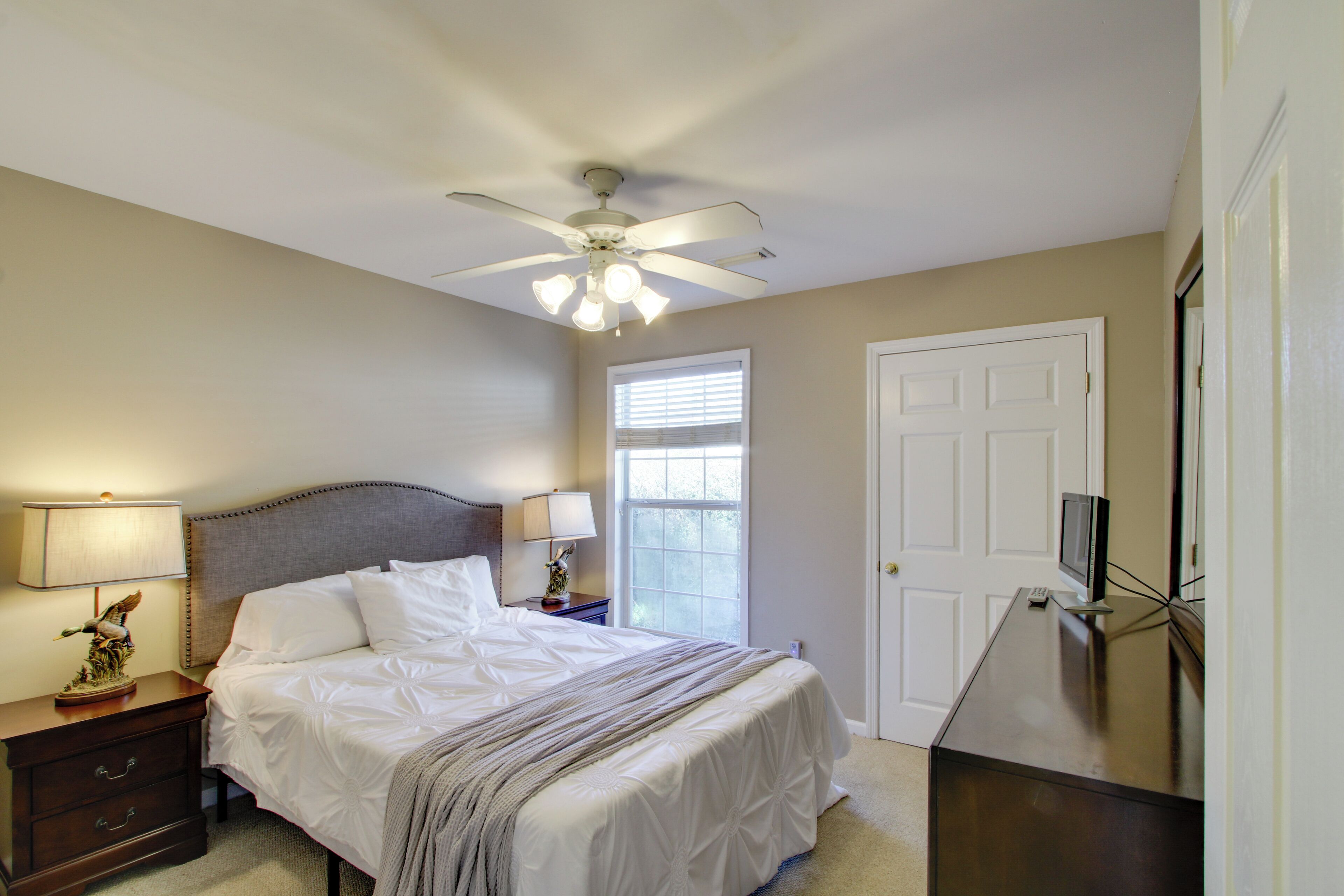 Une chambre à coucher comprenant un lit, des tables de chevet, un ventilateur de plafond, une fenêtre et un téléviseur.