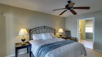 Une chambre à coucher comprenant un lit, deux tables de chevet avec des lampes, un ventilateur de plafond et une porte donnant sur une autre pièce.