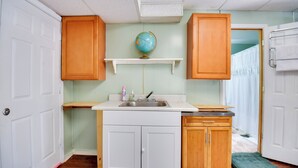 A compact kitchen with a sink, wooden cabinets, a globe on a shelf, and a door leading to another room.