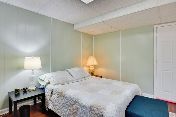 A bedroom with a bed, a nightstand with a lamp, a small table with a cup and a decorative item, and a door. - 4 Mi to Downtown: Wfh-friendly Loganville Studio (Loganville)