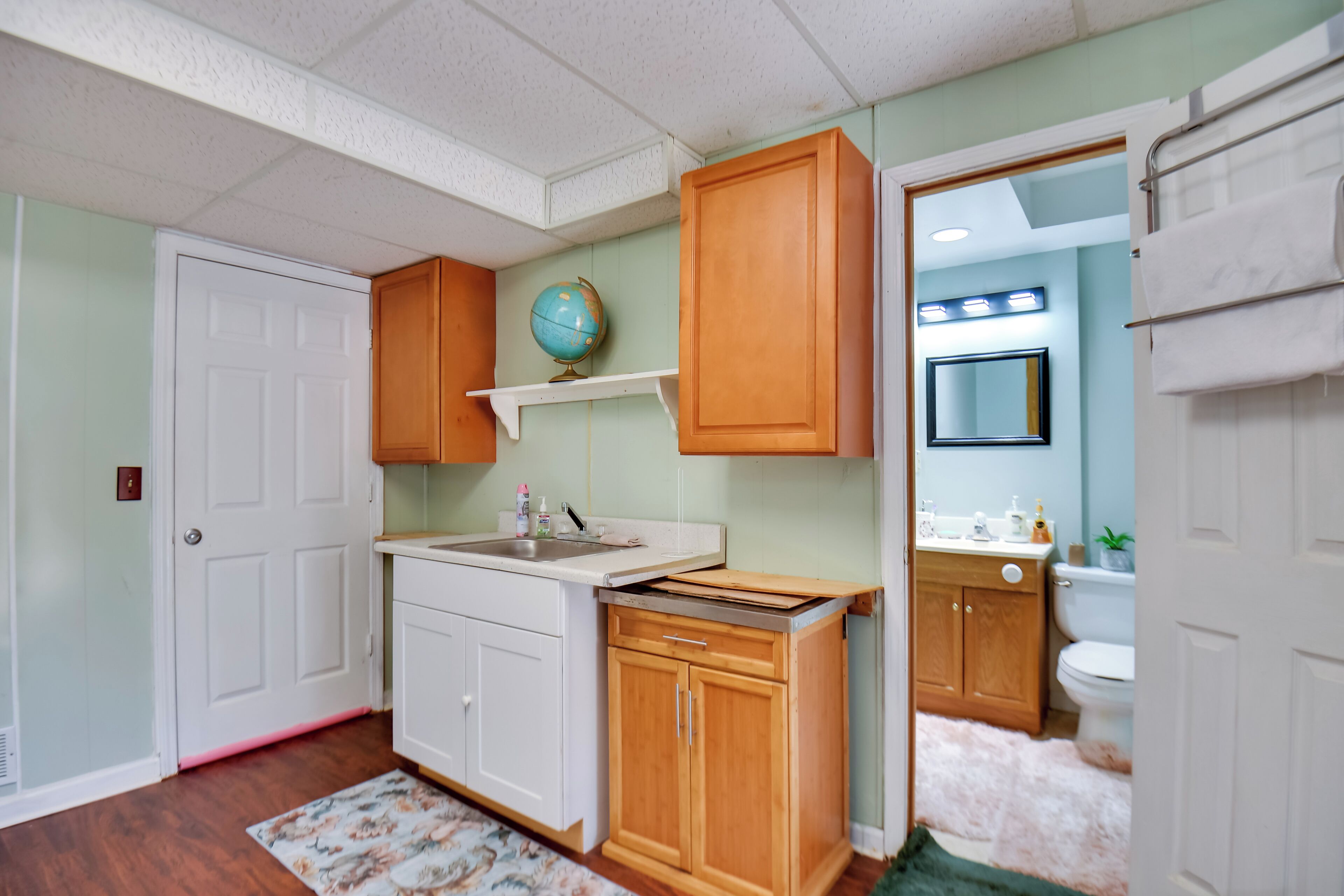 A compact kitchen with wooden cabinets, a white countertop, and a globe on a shelf.