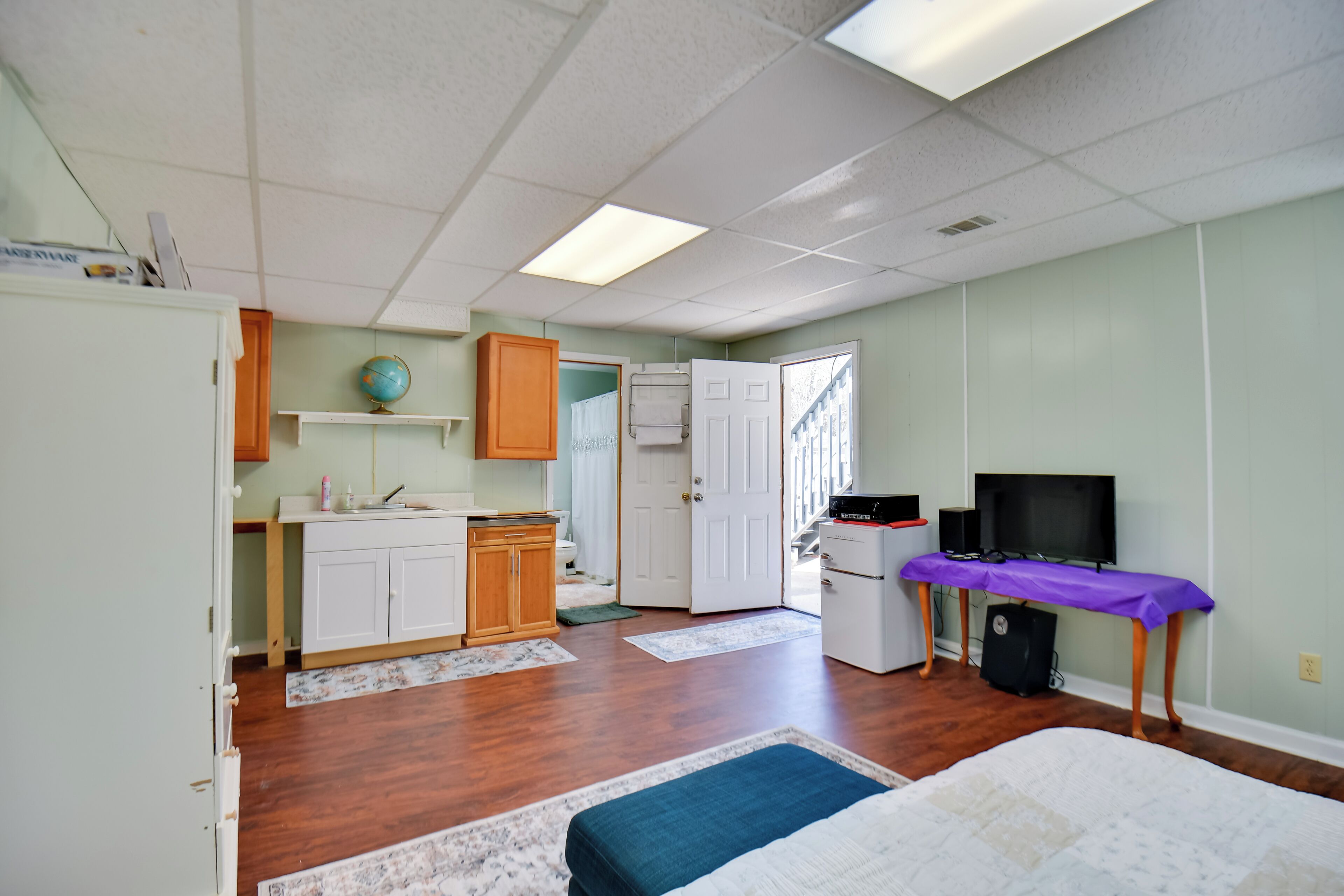 A compact room with a kitchenette, a bed, a television, and a desk.