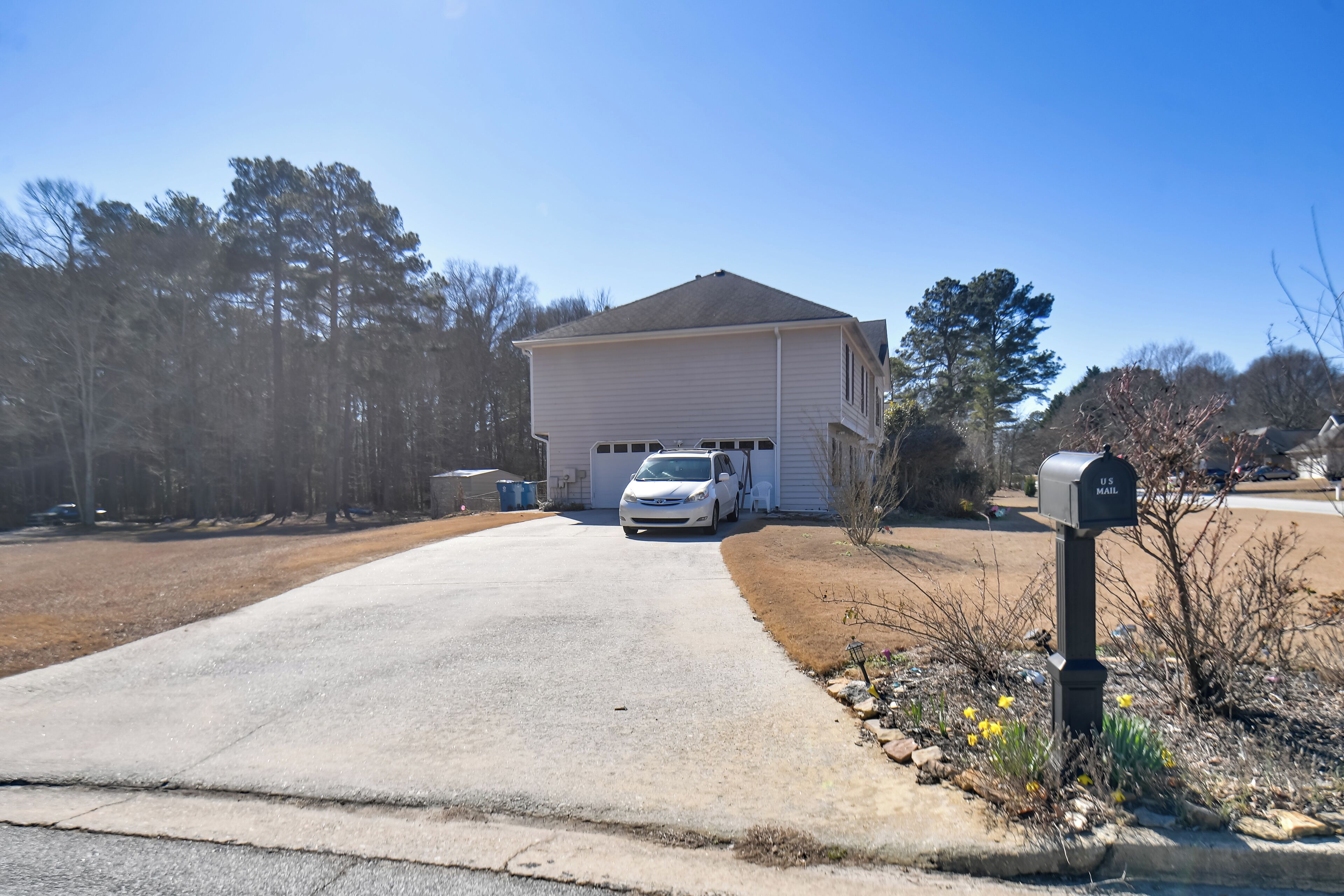 A single-story house with a driveway leading to the front door, a mailbox, and a parked car.