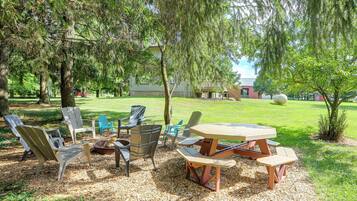 A patio area with outdoor furniture, including chairs and a table, surrounded by trees and a grassy lawn.