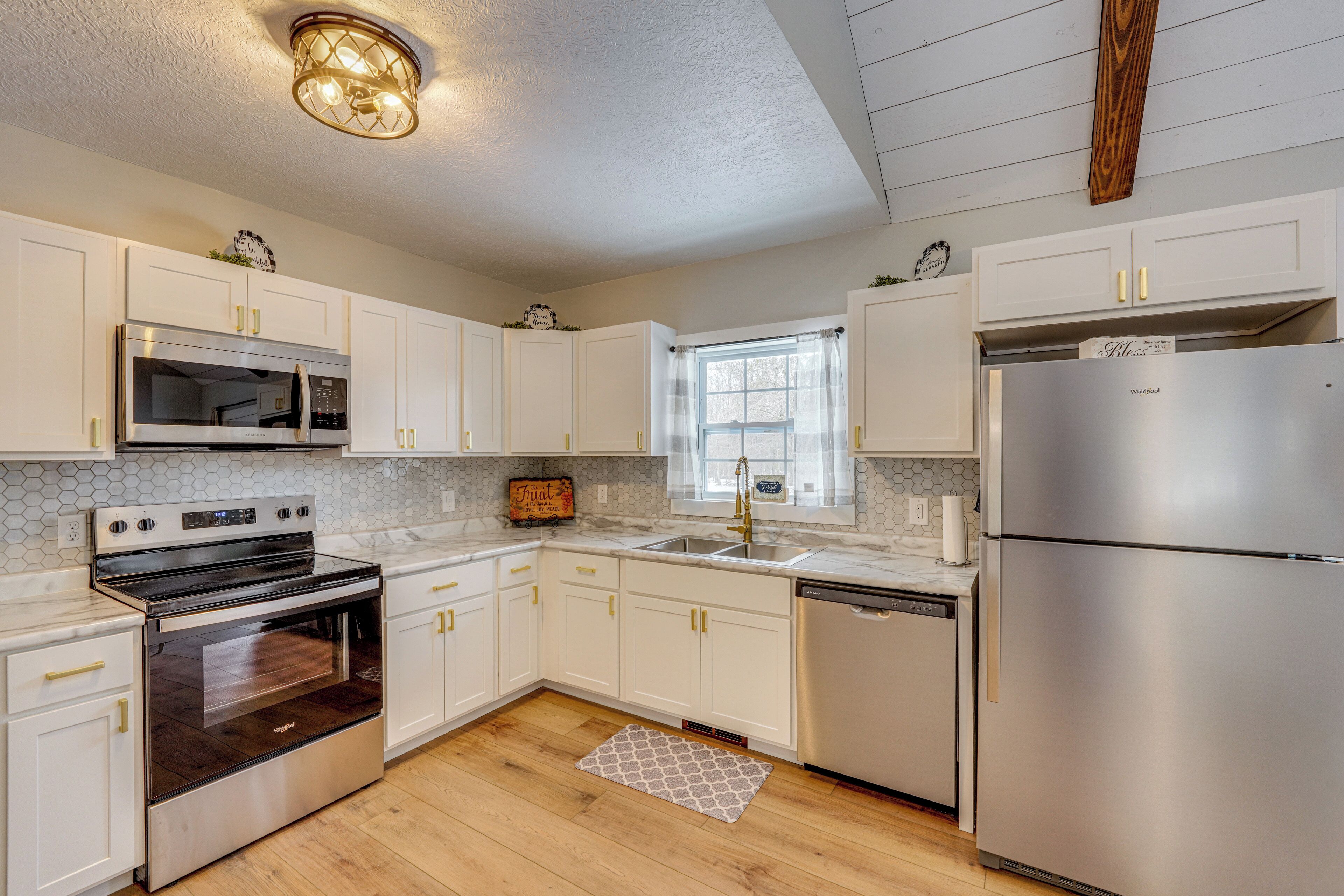 A modern kitchen with white cabinets, stainless steel appliances, a wooden floor, and a window with a view.