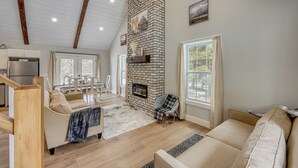 A spacious living area with a high ceiling, a fireplace, and a dining area with a table and chairs. - Willard Home On Working Farm w/ Water Views! (Willard)