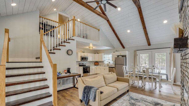 A spacious living area with a wooden staircase, a sofa, and a dining table with chairs. - Willard Home On Working Farm w/ Water Views! (Willard)