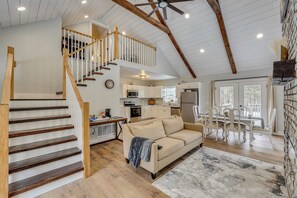 A spacious living area with a wooden staircase, a sofa, and a dining table with chairs. - Willard Home On Working Farm w/ Water Views! (Willard)