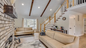 A spacious living room with a fireplace, two sofas, a staircase, and a dining area. - Willard Home On Working Farm w/ Water Views! (Willard)