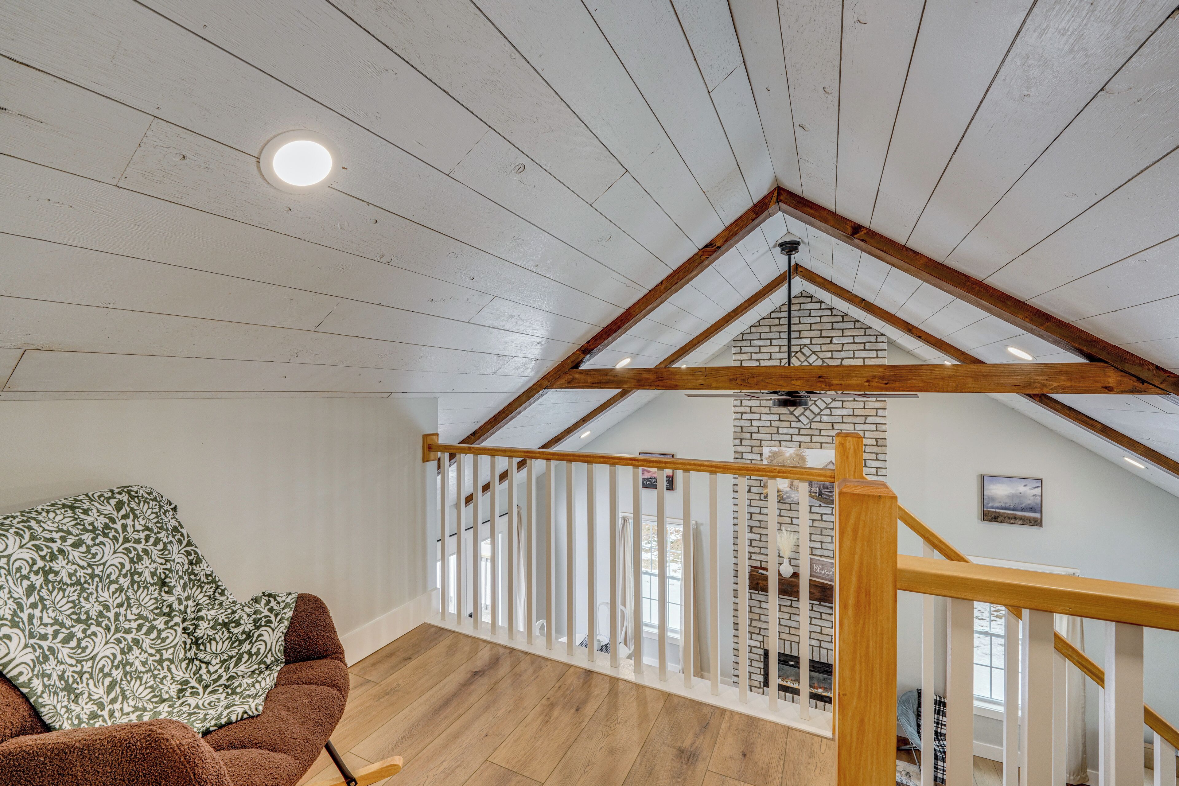 Un espacio tipo loft con vigas de madera a la vista, pared de ladrillo y vistas al exterior.