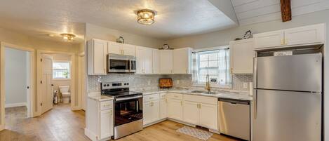 A modern kitchen with white cabinets, stainless steel appliances, and a wooden floor.