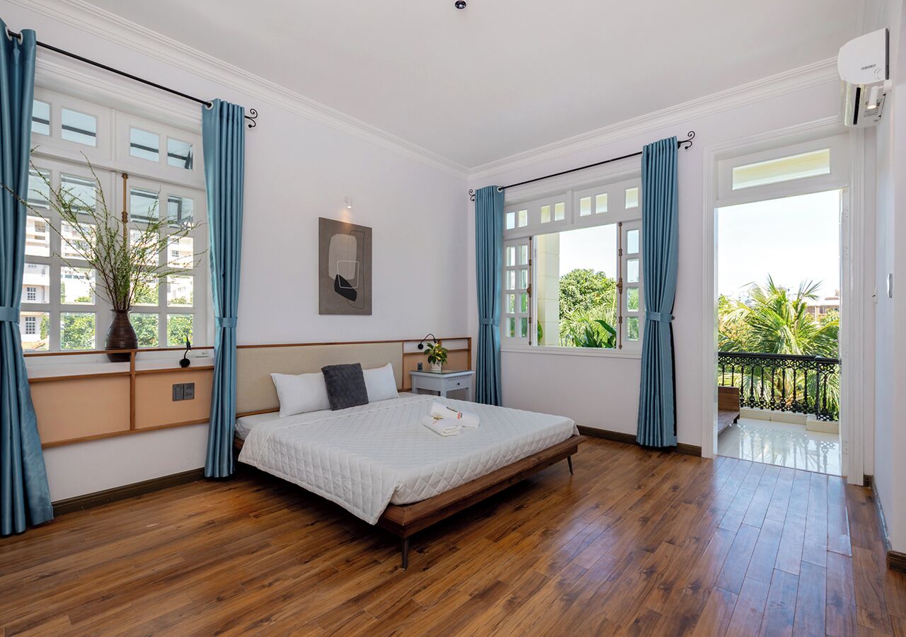 Een ruime slaapkamer met een groot bed, houten vloeren en een balkon met uitzicht op groen.