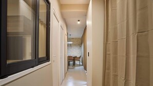 Un corridoio stretto con una finestra a sinistra, una porta a destra e una sala da pranzo in fondo.