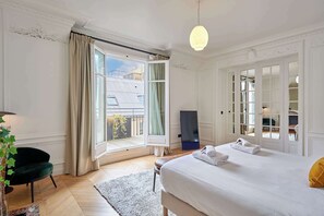 Een slaapkamer met een groot bed, een raam met gordijnen, een bureau en een stoel.