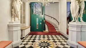 Un amplio pasillo con piso a cuadros, una puerta verde y una escalera con peldaños rojos.