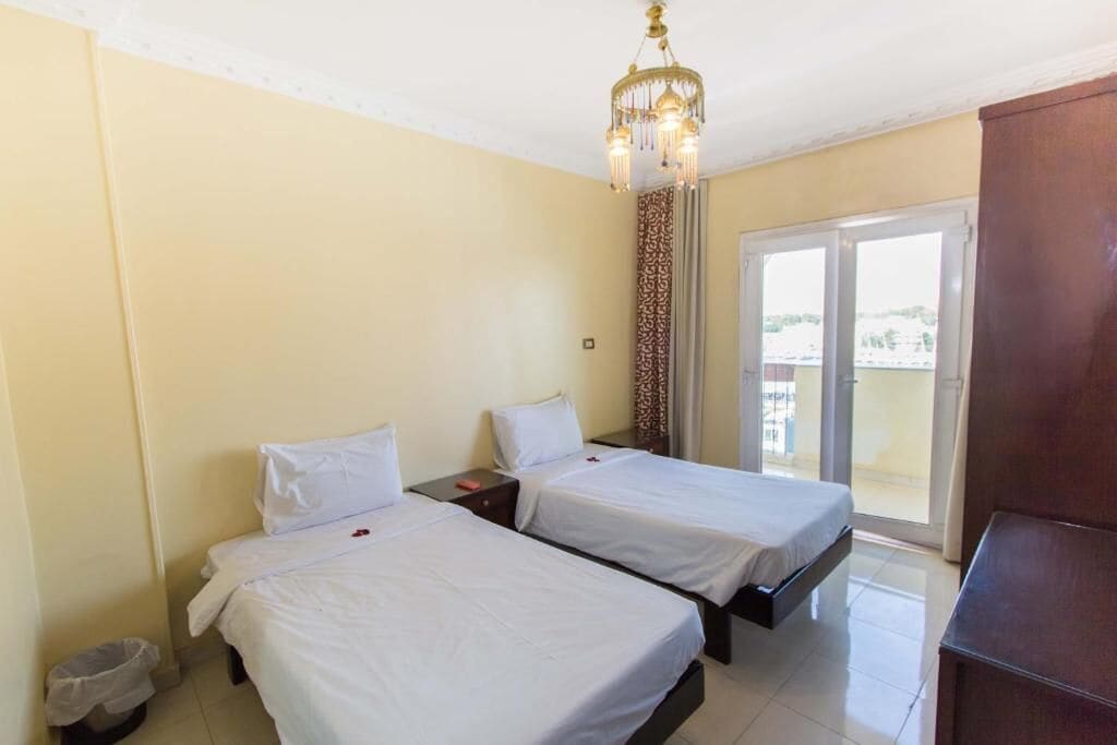 Habitación de hotel con dos camas, un candelabro, una puerta corredera de vidrio al balcón y un cesto de basura pequeño.