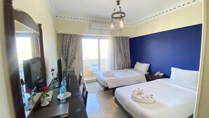 A hotel room with two beds, a desk with a mirror, a chandelier, and a view of the outside through a sliding door. - Philae Hotel (Aswan)