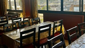 A restaurant with multiple tables and chairs, large windows with a view of a harbor and buildings. - Philae Hotel (Aswan)