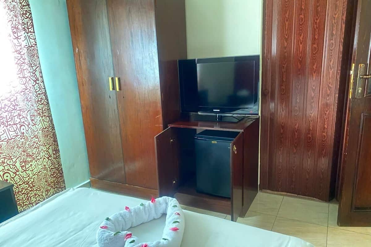Een hotelkamer met een bed, een televisie, een kledingkast en een klein bureau met een koelkast.