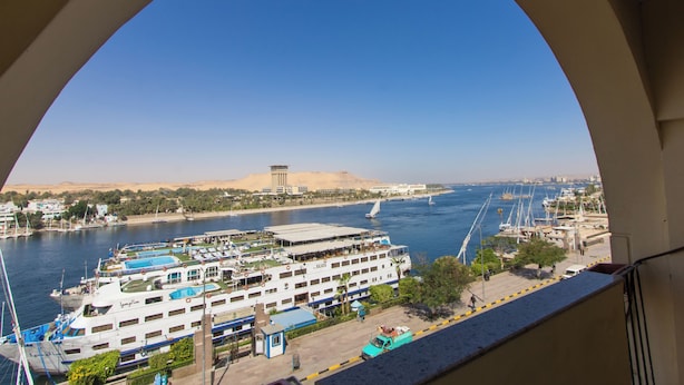 A river view with a large cruise ship docked, a sandy landscape, and a clear blue sky. - Philae Hotel (Aswan)