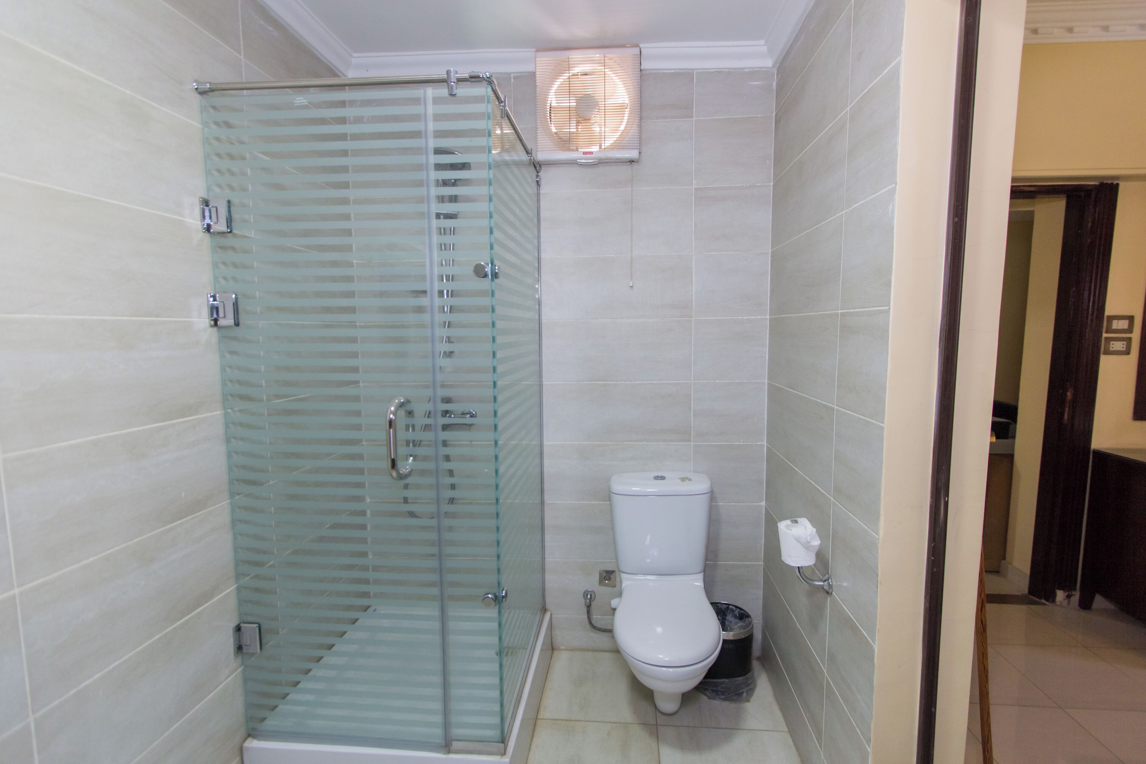 A bathroom with a glass-enclosed shower, a toilet, and a wall-mounted fan.