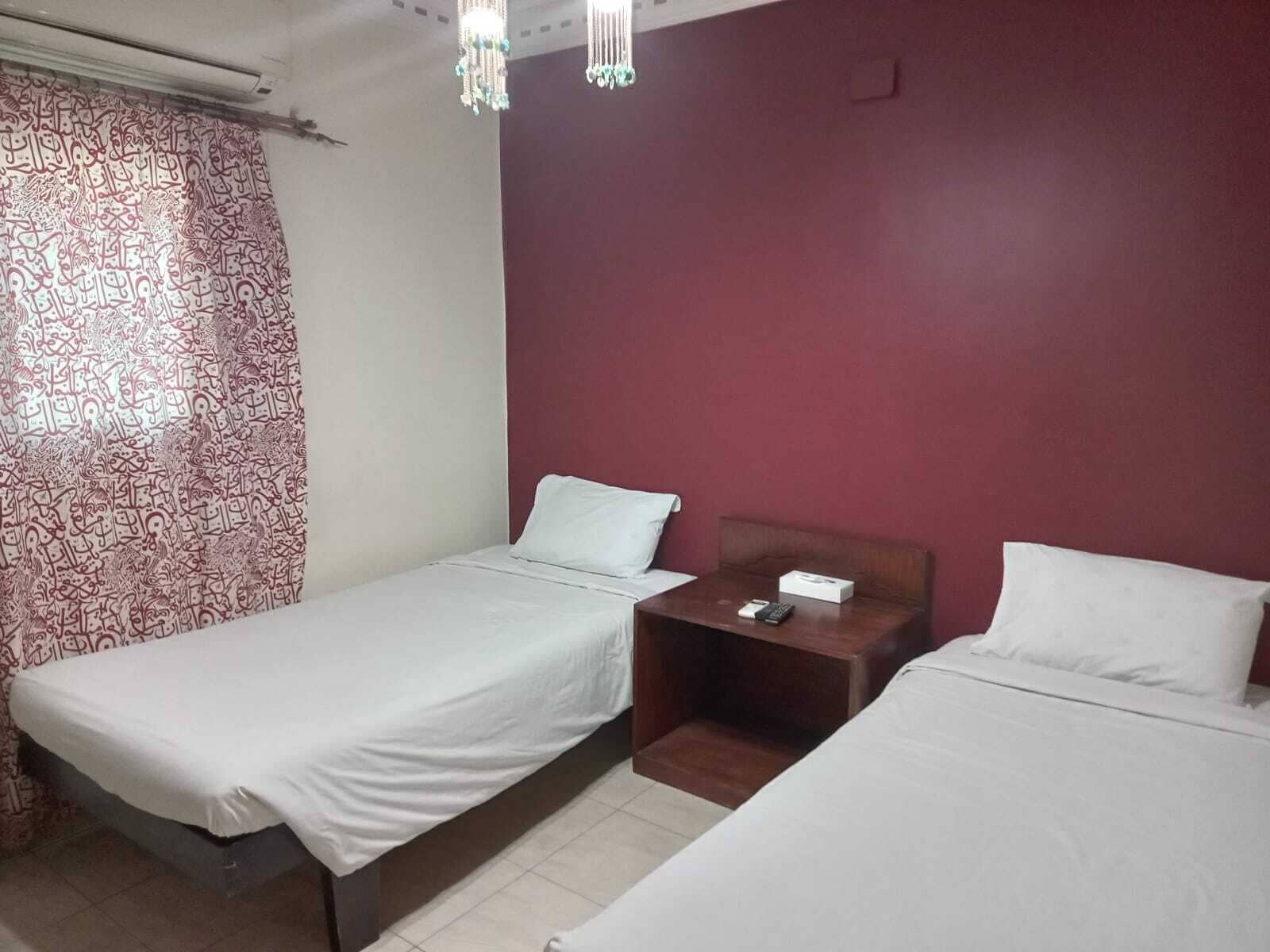 Quarto com duas camas de solteiro, mesa de cabeceira com controle remoto e cortina estampada.