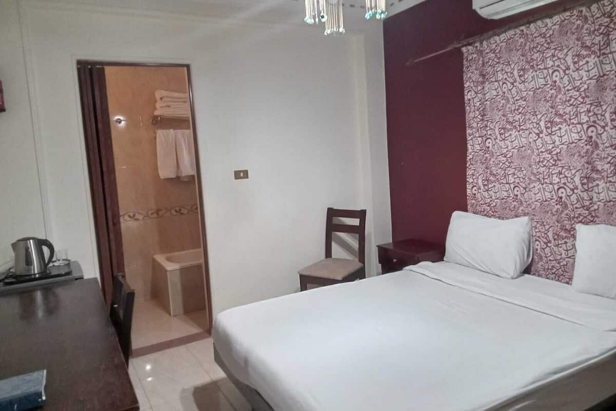 Een hotelkamer met een bed, een stoel, een bureau met waterkoker en een airconditioning.