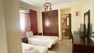 A hotel room with two beds, a desk, a TV, and a bathroom visible through an open door.