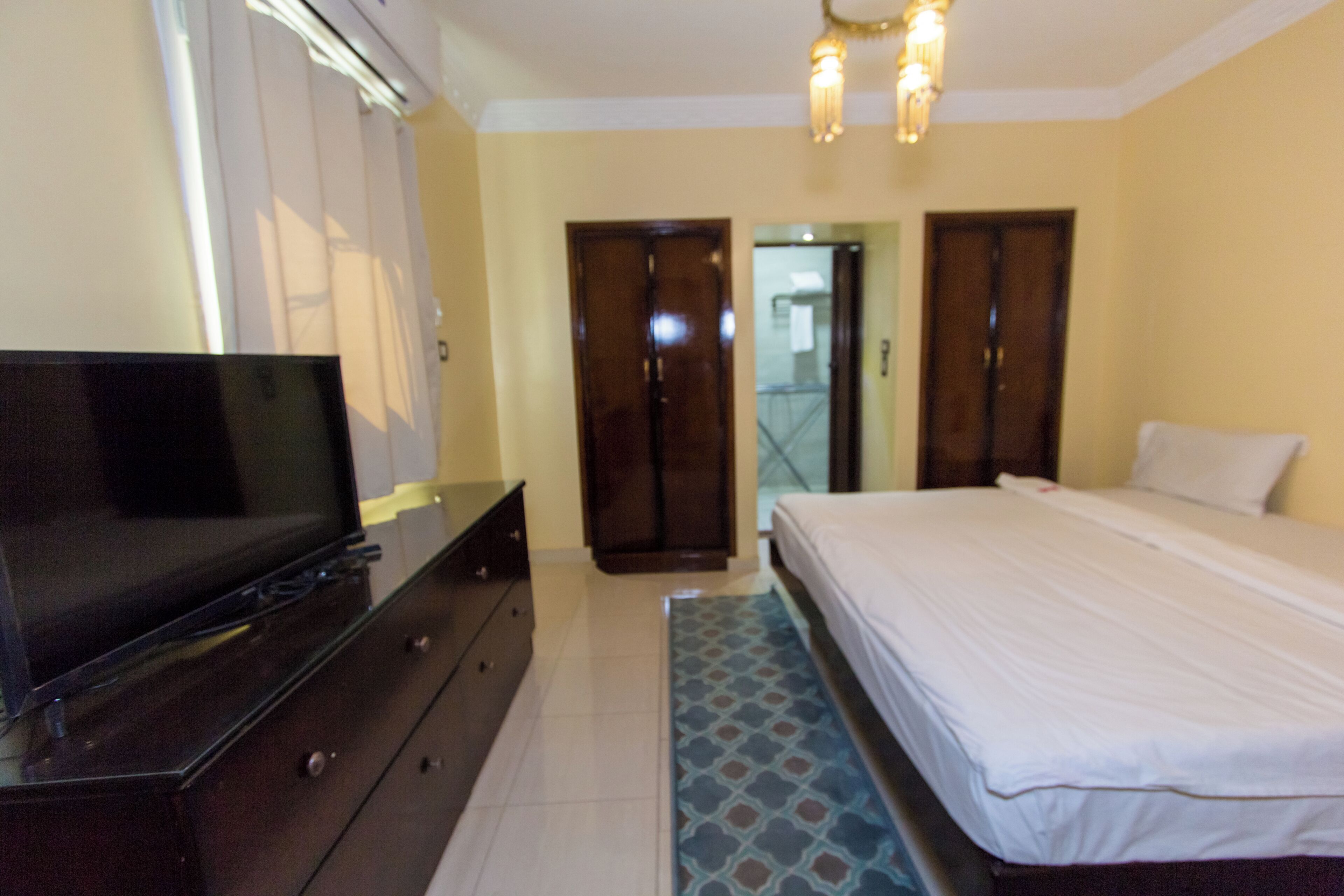 A bedroom with a bed, a dresser, a television, and a patterned rug.
