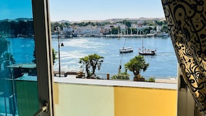 A view from a balcony overlooking a harbor with boats, palm trees, and buildings in the background. - Philae Hotel (Aswan)
